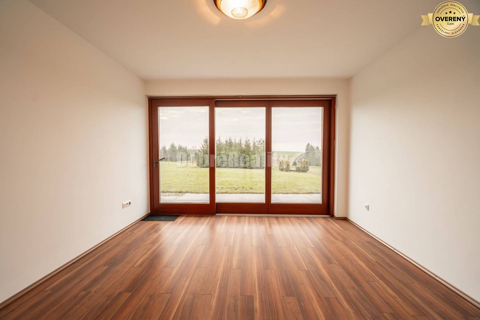 Izba v rodinnom dome s podlahou s dreveným dekorom a výhľadom na záhradu.