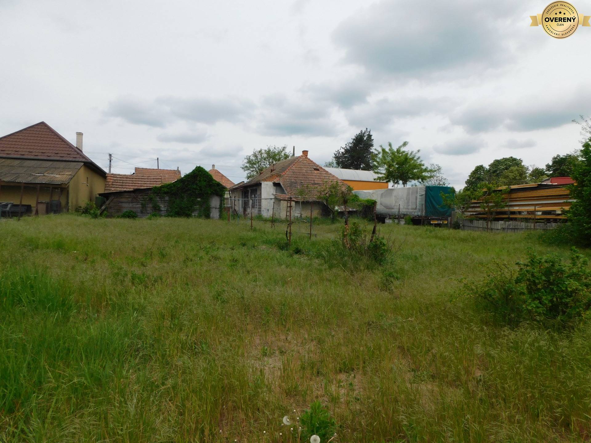Pozemky na bývanie v Dvoroch nad Žitavou s vidieckymi stavbami a hustou trávou.