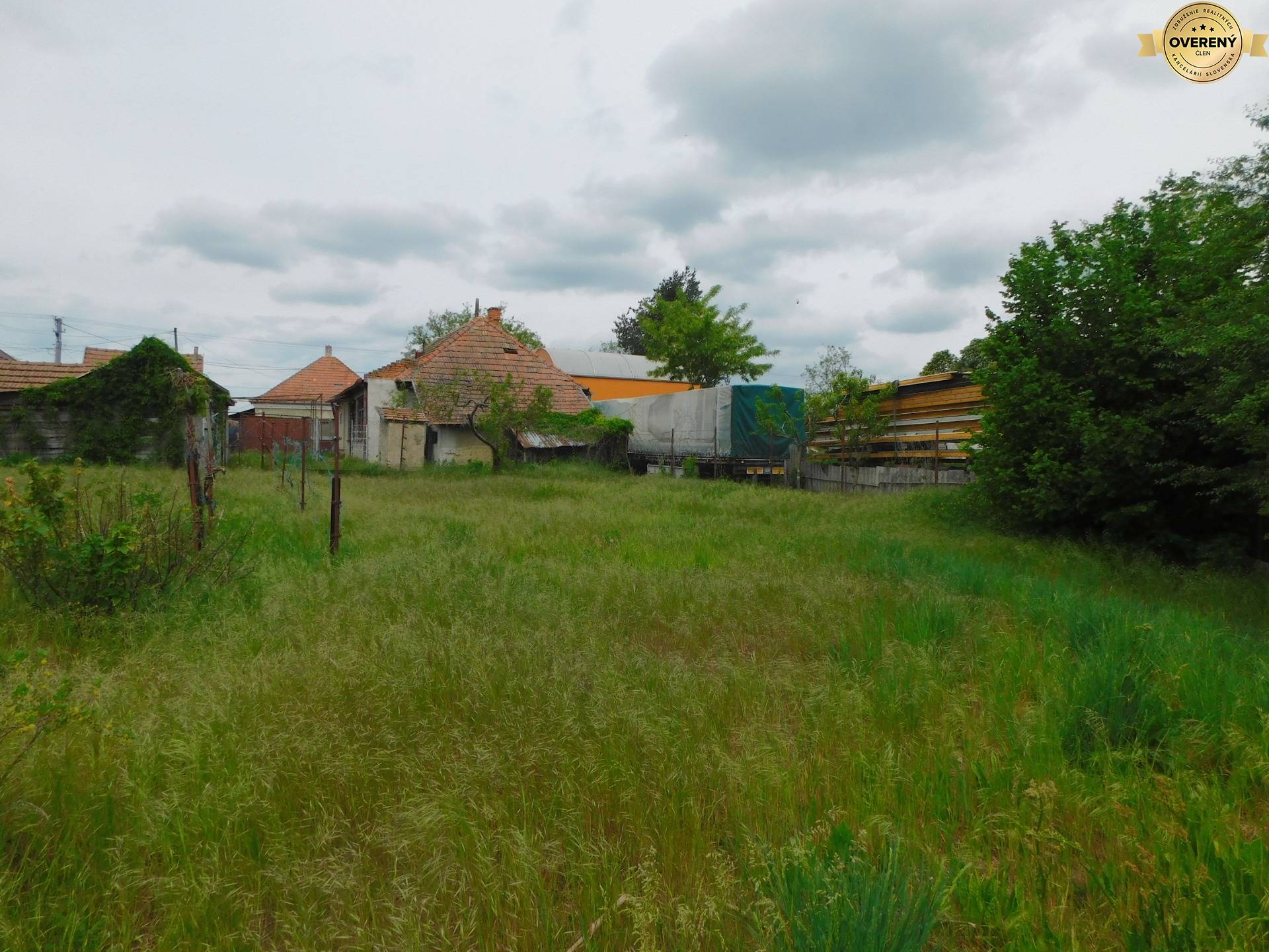 Zelená záhrada s budovami v pozadí v Dvory nad Žitavou, ideálna na pozemky - bývanie.